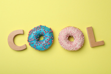 Photo of Word COOL made with wooden letters and donuts on yellow background, flat lay