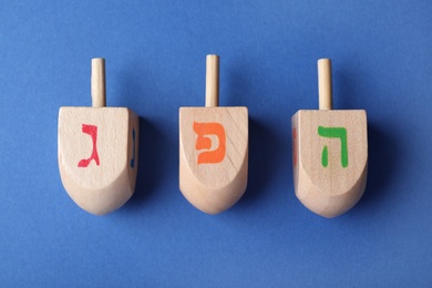Hanukkah traditional dreidels with letters Gimel, He and Pe on blue background, flat lay
