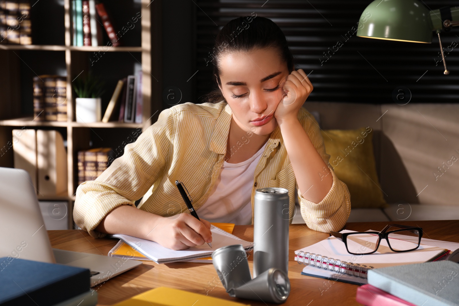 Photo of Tired young woman with energy drink studying at home