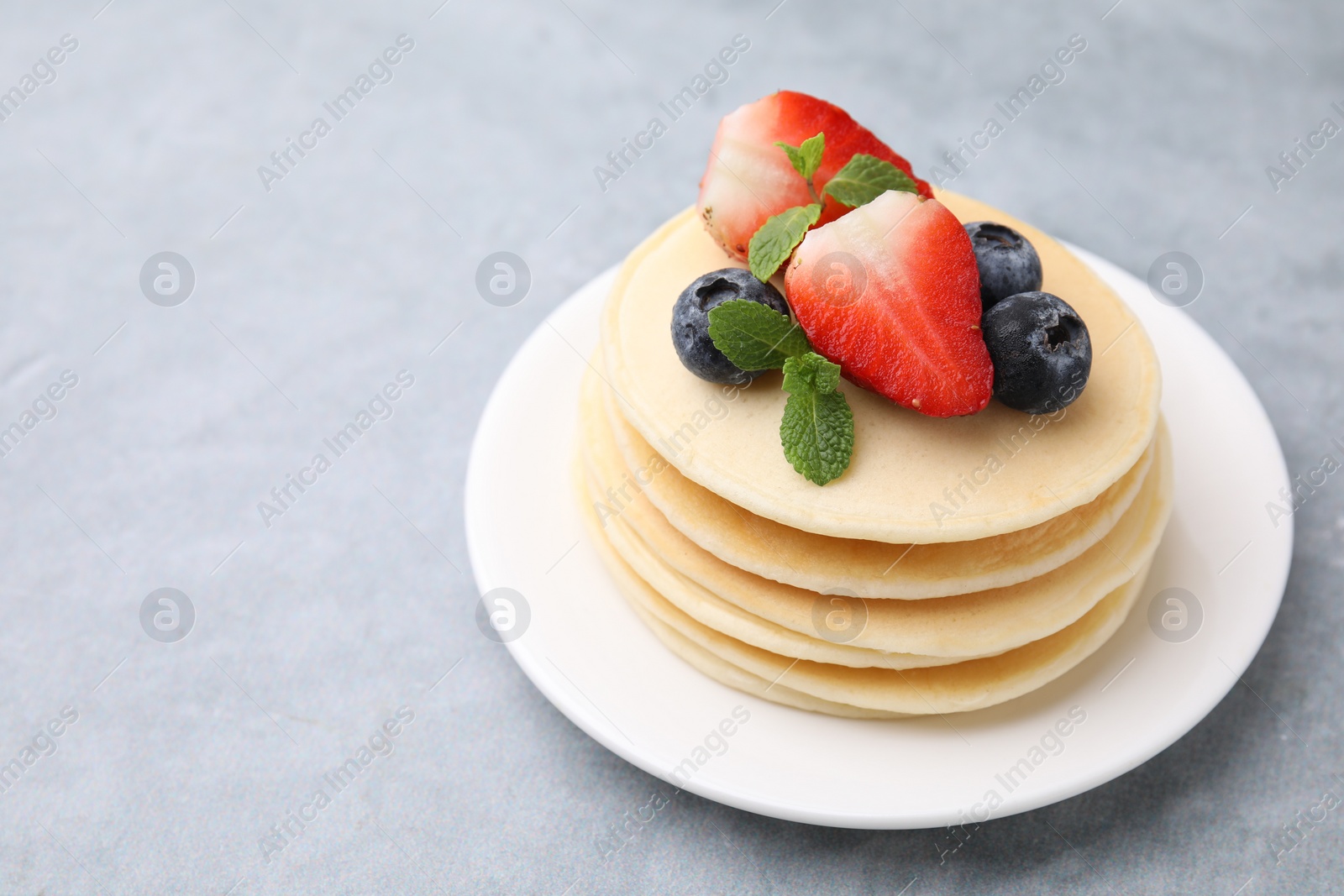 Photo of Stack of tasty pancakes with fresh berries and mint on light grey table, closeup. Space for text