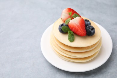 Photo of Stack of tasty pancakes with fresh berries and mint on light grey table, closeup. Space for text