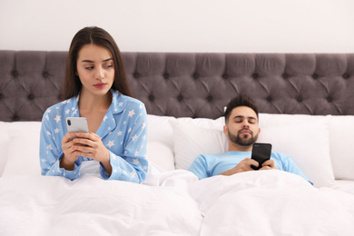 Photo of Young couple with smartphones in bed at home