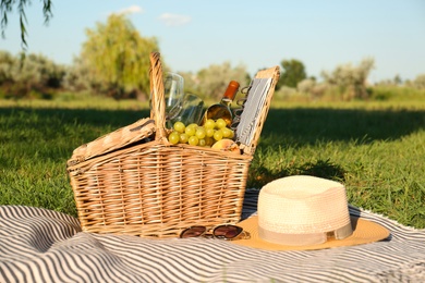 Picnic basket with snacks and bottle of wine on blanket in park