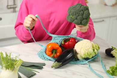 Photo of Woman taking broccoli out from string bag at light marble table, closeup