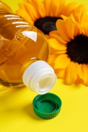 Photo of Bottle of cooking oil and sunflowers on yellow background, closeup