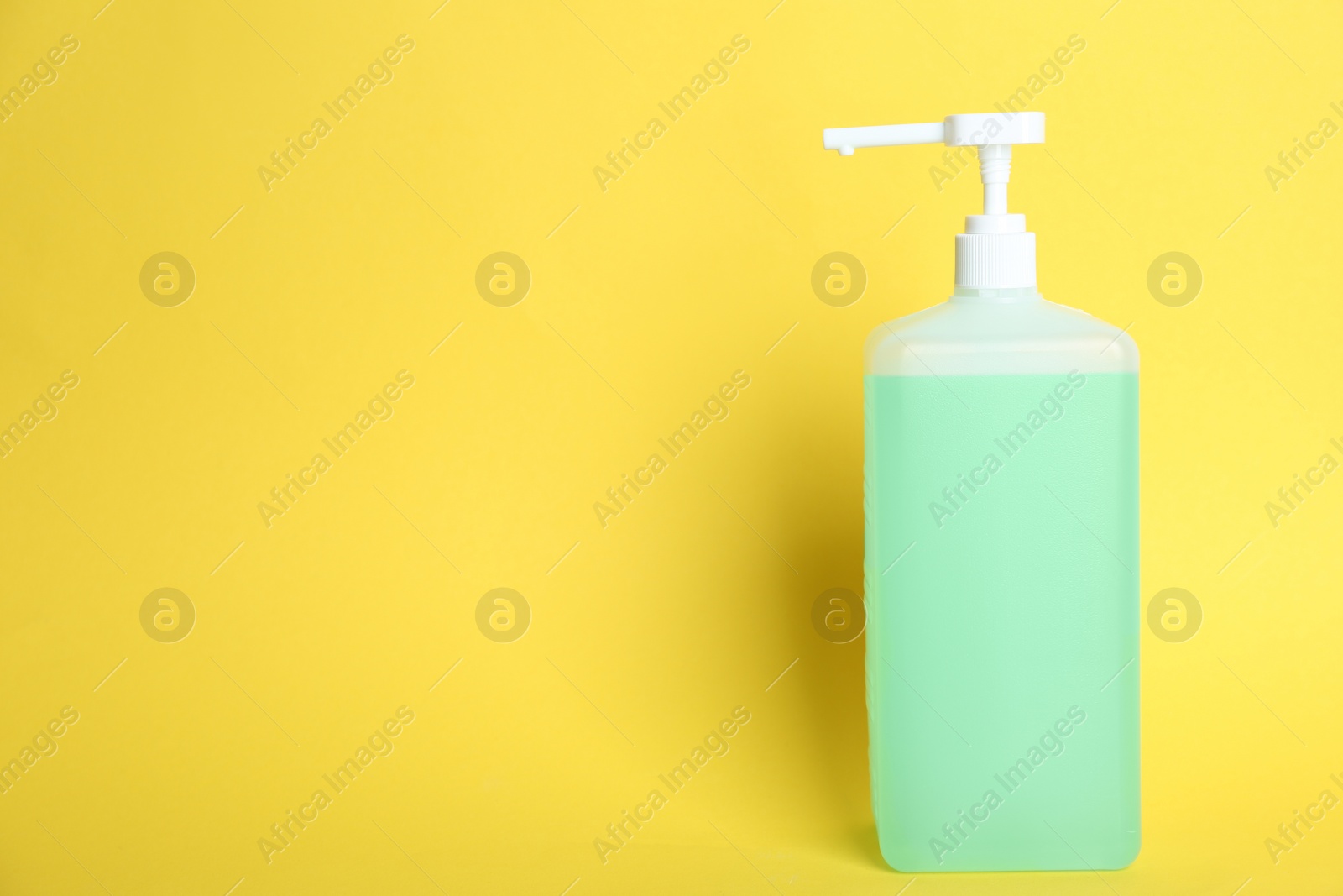 Photo of Dispenser bottle with green antiseptic gel on yellow background. Space for text