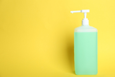 Dispenser bottle with green antiseptic gel on yellow background. Space for text