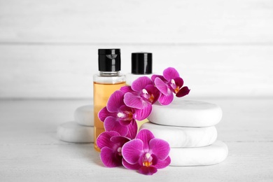 Photo of Spa stones, bottles and orchid flowers on white wooden table