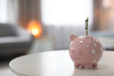Photo of Piggy bank with money on table against blurred background. Space for text