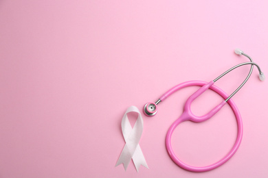 Photo of Pink ribbon and stethoscope on color background, flat lay with space for text. Breast cancer concept