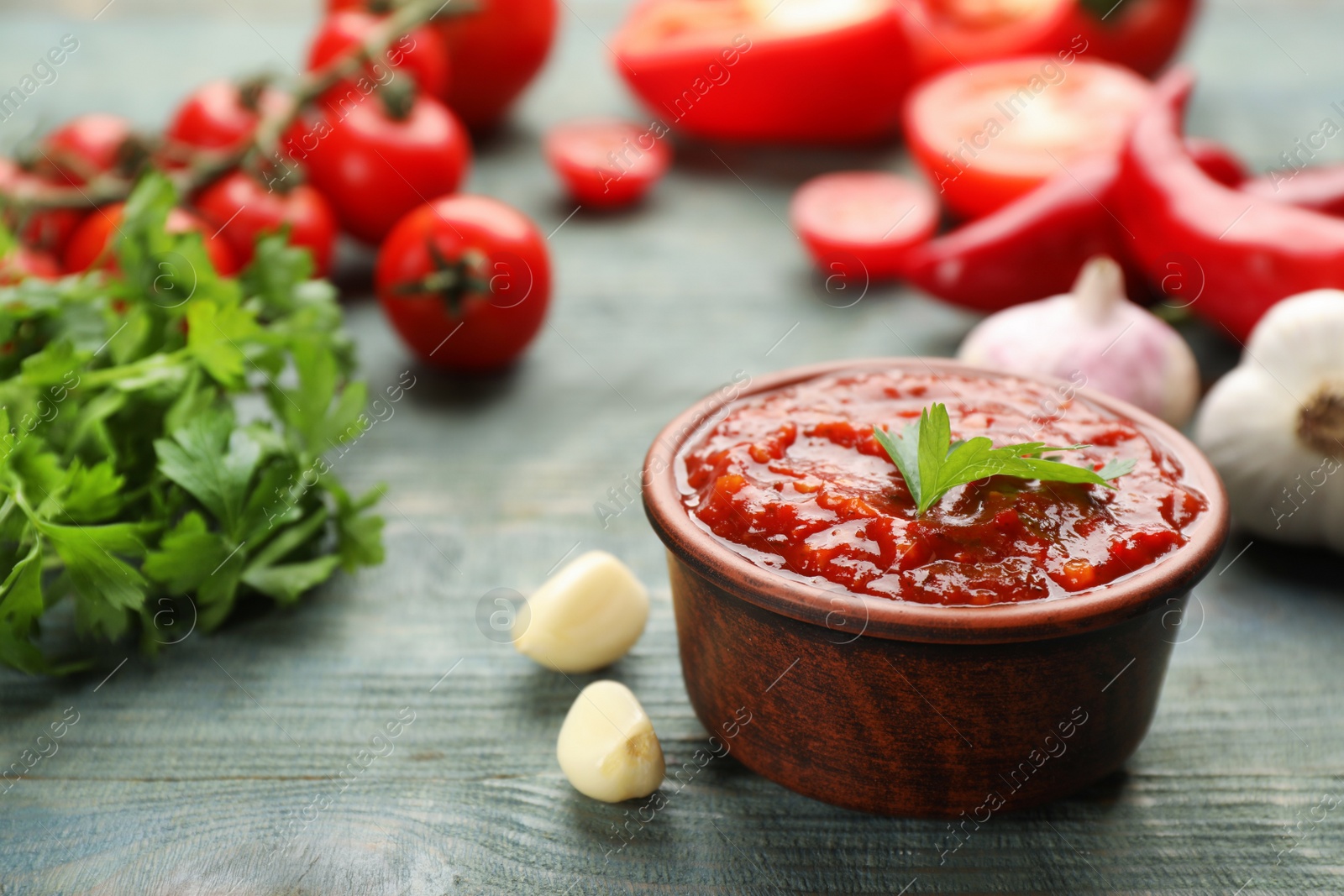 Photo of Delicious adjika sauce in bowl and ingredients on light blue wooden table