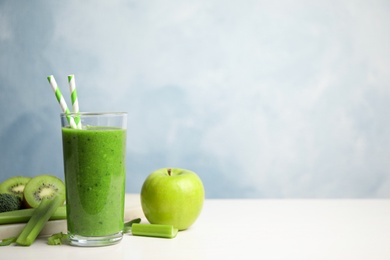Photo of Delicious green juice and fresh ingredients on white table against light blue background, space for text