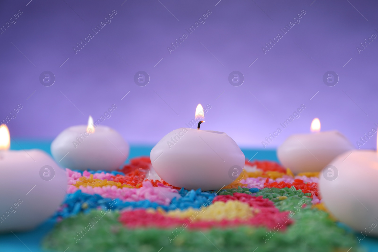 Photo of Diwali celebration. Burning candles and colorful rangoli against purple background, closeup