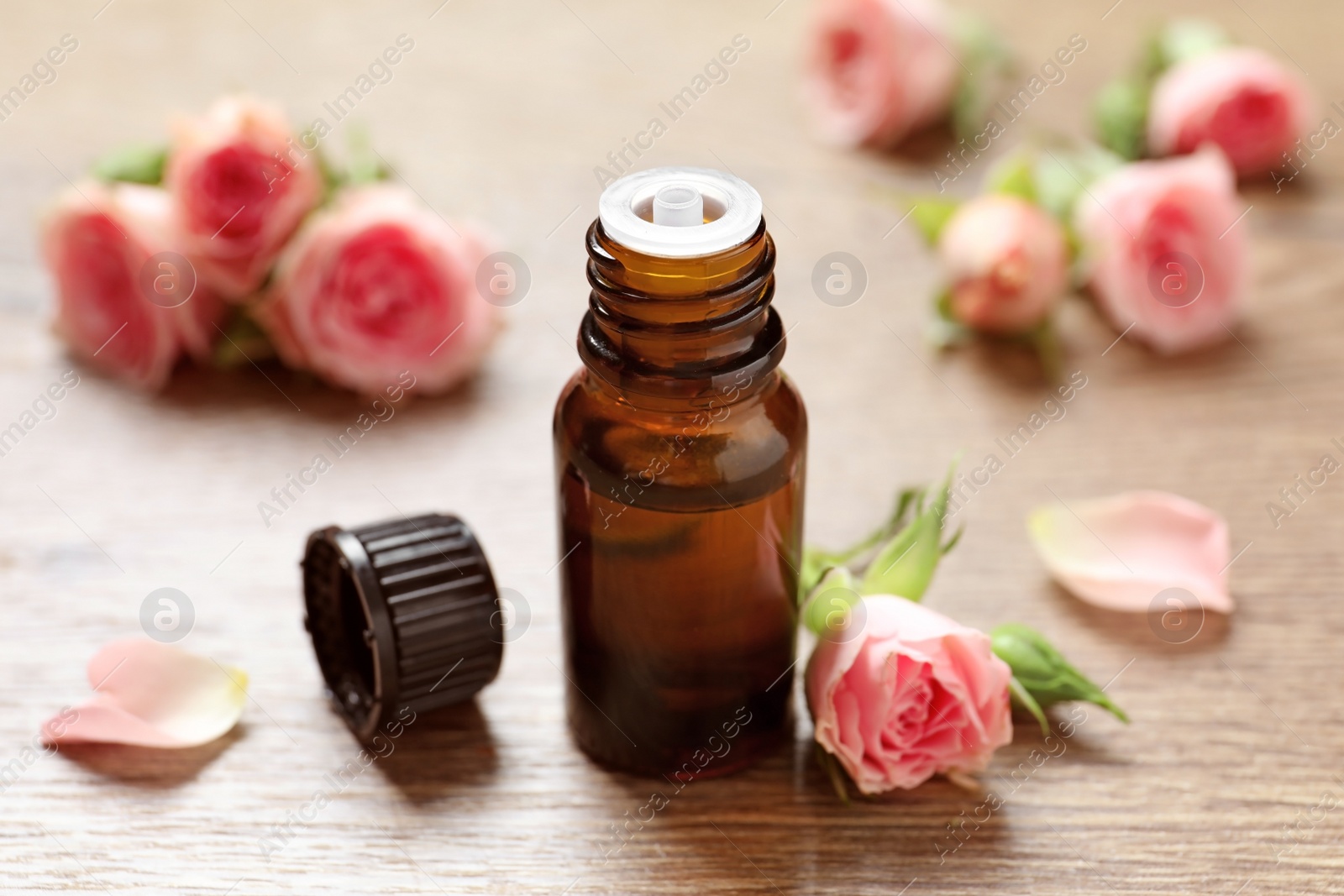 Photo of Bottle of rose essential oil and fresh flowers on wooden table