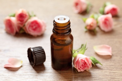 Photo of Bottle of rose essential oil and fresh flowers on wooden table