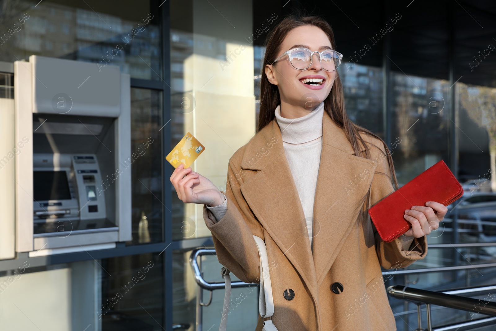 Photo of Excited young woman with credit card near cash machine outdoors