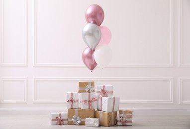 Photo of Many gift boxes and balloons near white wall in room