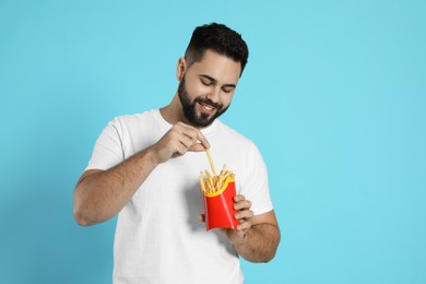 Young man with French fries on light blue background
