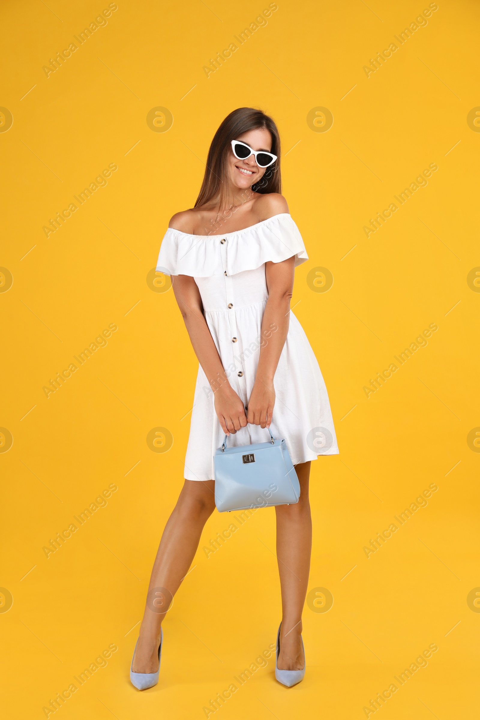 Photo of Young woman wearing stylish white dress with elegant bag on yellow background