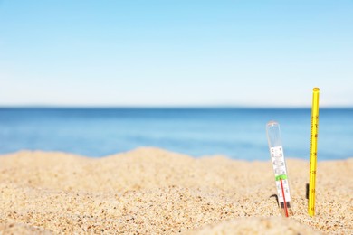 Photo of Weather thermometers in sand near sea, space for text