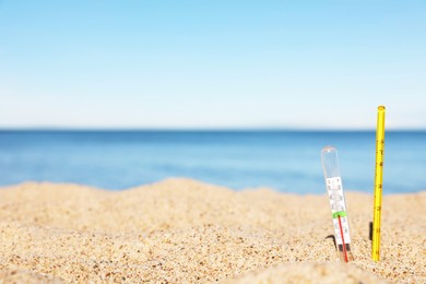 Weather thermometers in sand near sea, space for text