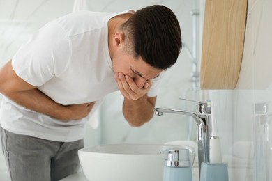 Photo of Man suffering from nausea near sink in bathroom. Food poisoning
