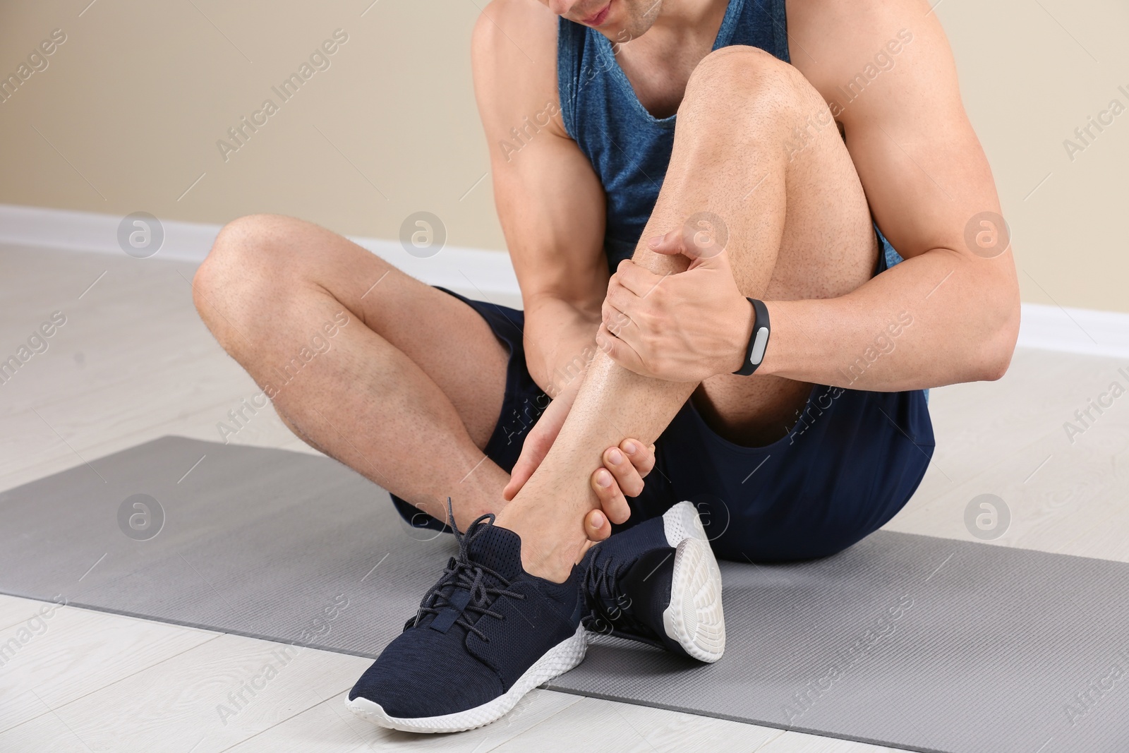 Photo of Male athlete suffering from leg pain during training indoors