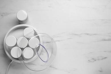 Modern yogurt maker with jars on white marble table, flat lay. Space for text