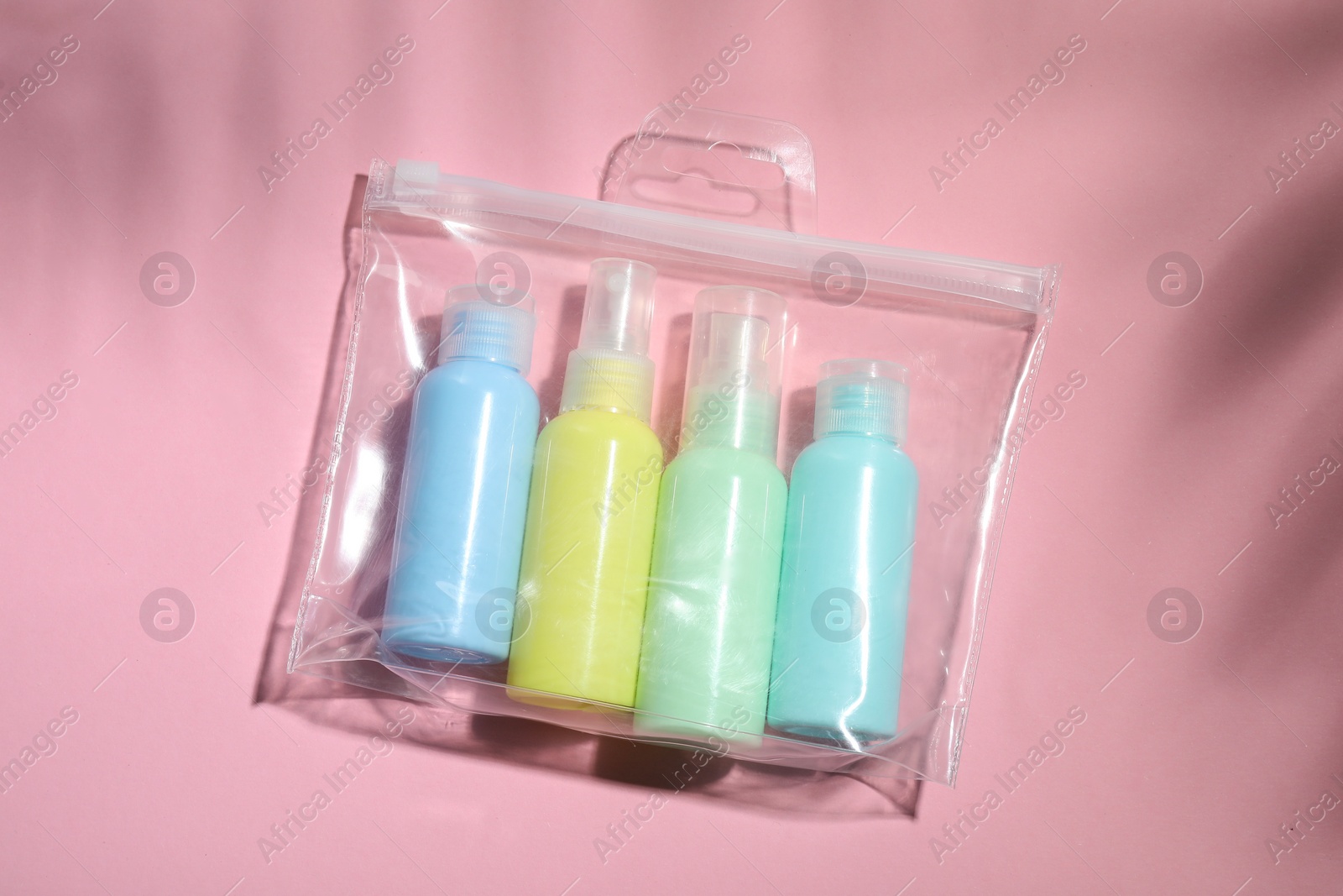 Photo of Cosmetic travel kit in plastic bag on pink background, top view. Bath accessories