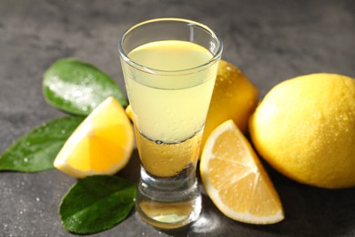 Photo of Tasty limoncello liqueur, lemons and green leaves on grey table, closeup