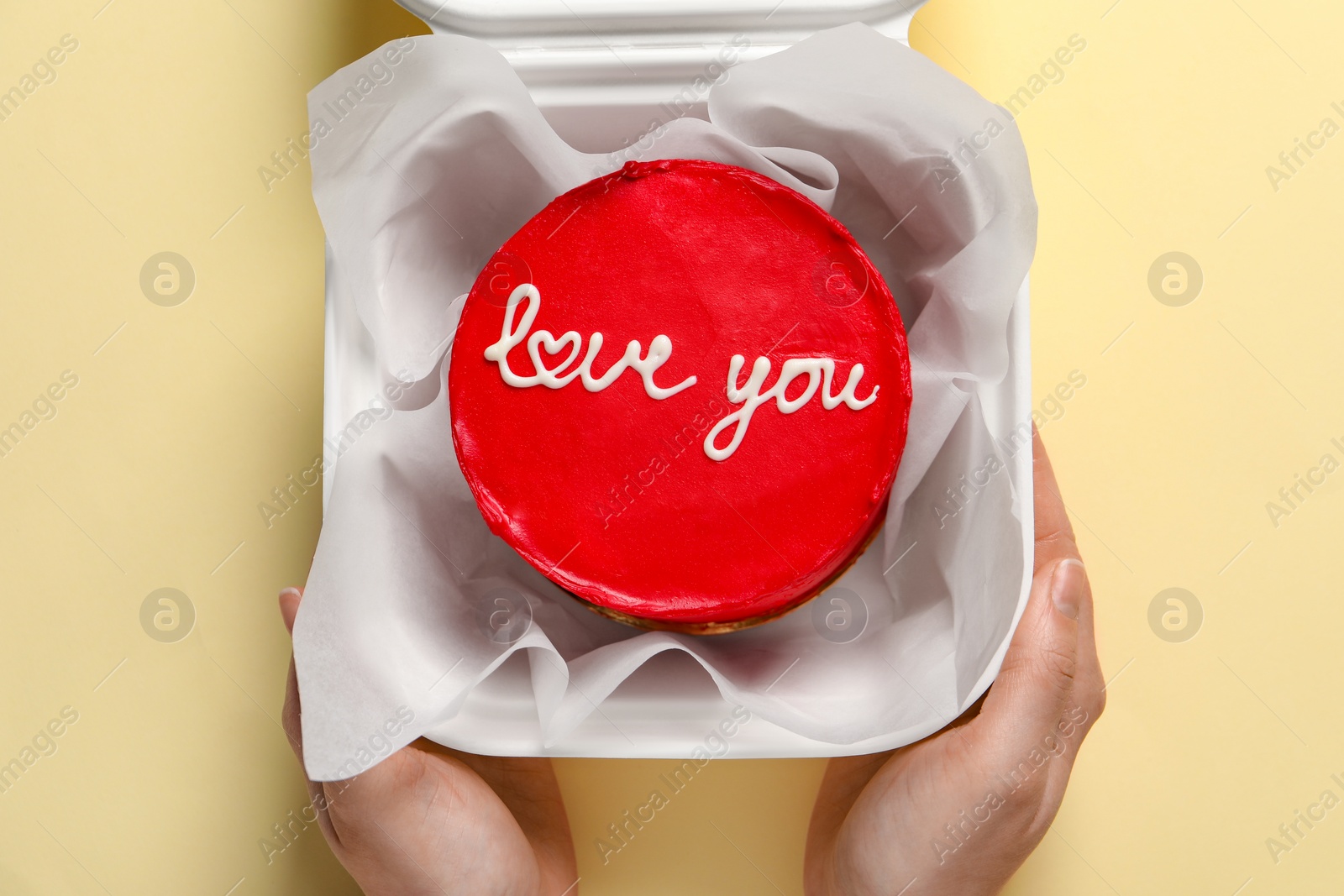 Photo of Woman holding takeaway box with bento cake at beige table, top view. St. Valentine's day surprise