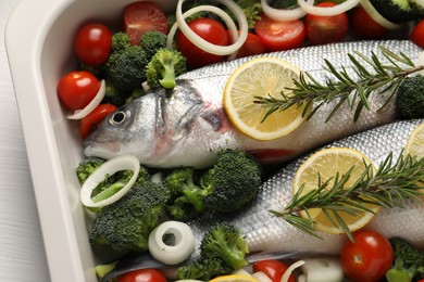 Photo of Raw fish with vegetables and lemon in baking dish on white table