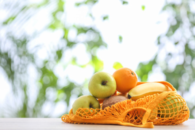 Net bag with fruits on table against blurred background, space for text