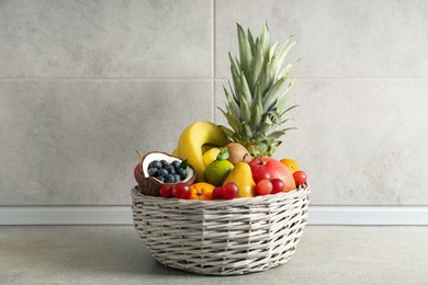 Photo of Assortment of fresh exotic fruits in wicker basket on grey table