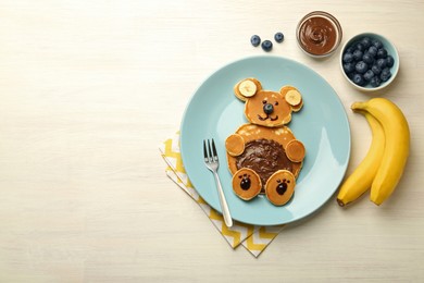 Creative serving for kids. Plate with cute bear made of pancakes, blueberries, bananas and chocolate paste on light wooden table, flat lay. Space for text