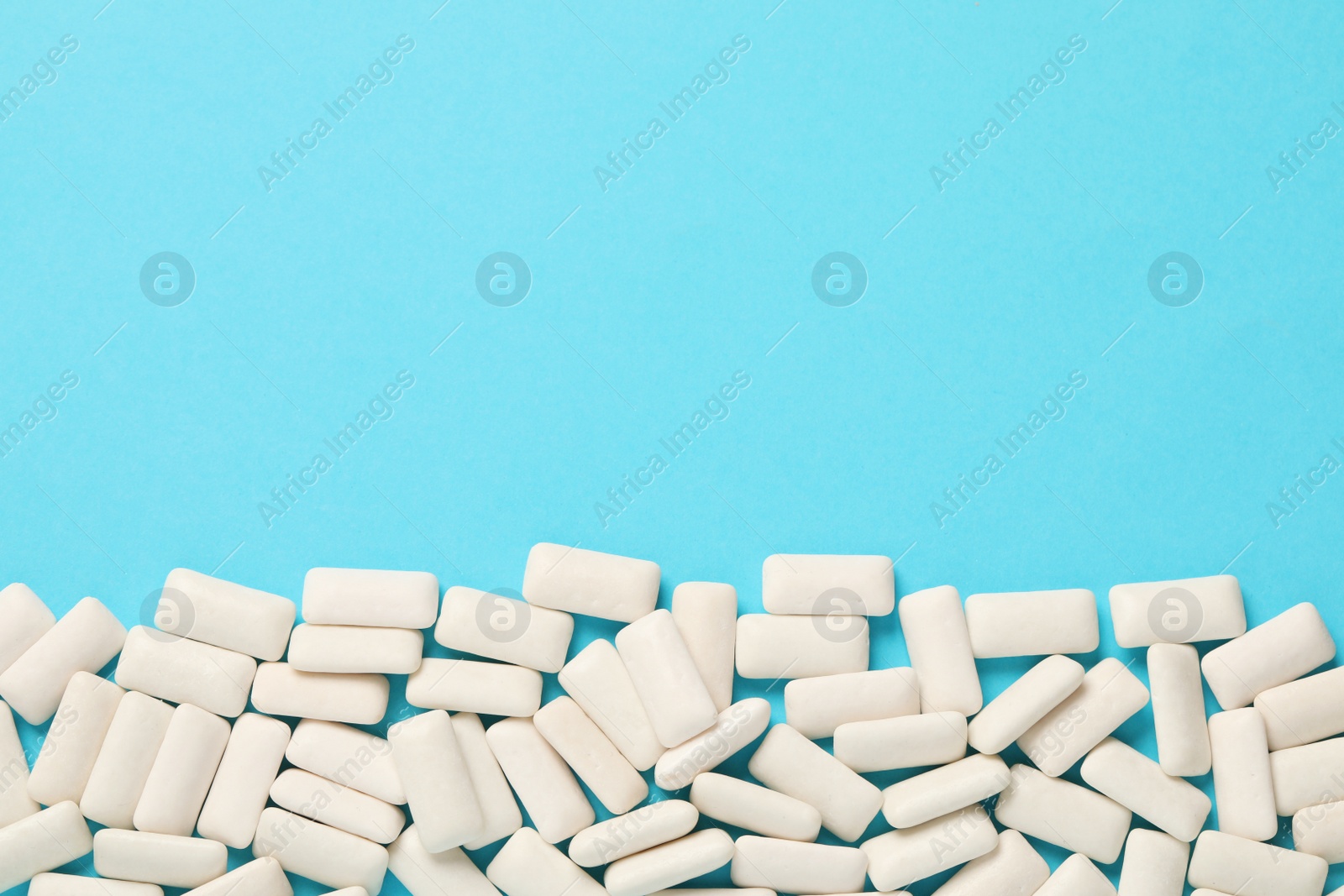 Photo of Many chewing gum pieces on light blue background, flat lay. Space for text
