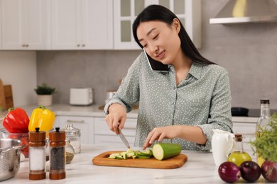 Photo of Smiling woman talking by smartphone while cooking in kitchen