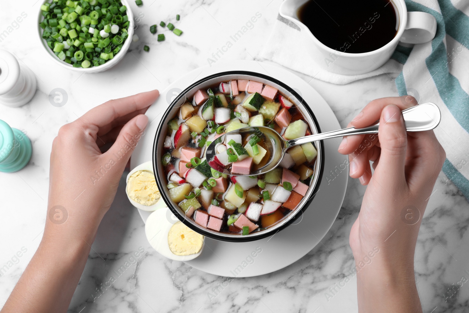 Photo of Woman eating delicious cold okroshka with kvass at white marble table, top view. Traditional Russian summer soup