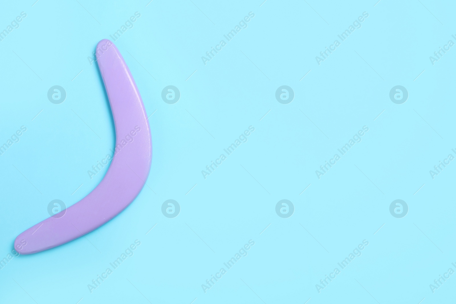 Photo of Lilac wooden boomerang on light blue background, top view. Space for text