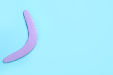 Lilac wooden boomerang on light blue background, top view. Space for text