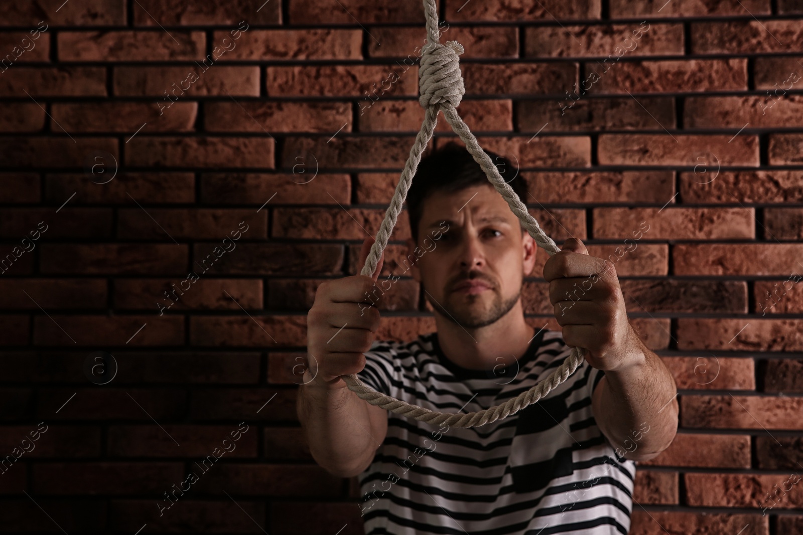 Photo of Depressed man with rope noose near brick wall