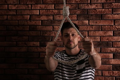 Photo of Depressed man with rope noose near brick wall