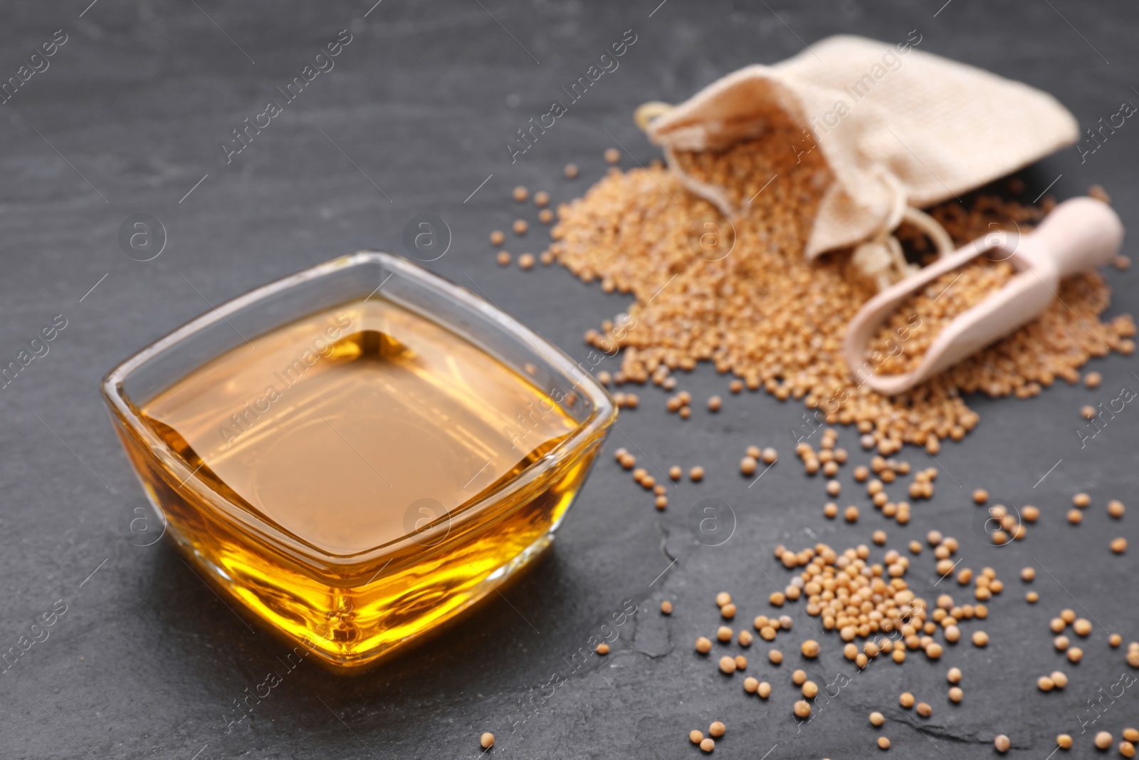 Bowl with natural oil and mustard seeds on black table. Space for text Photo of Bowl with natural oil and mustard seeds on black table. Space for text