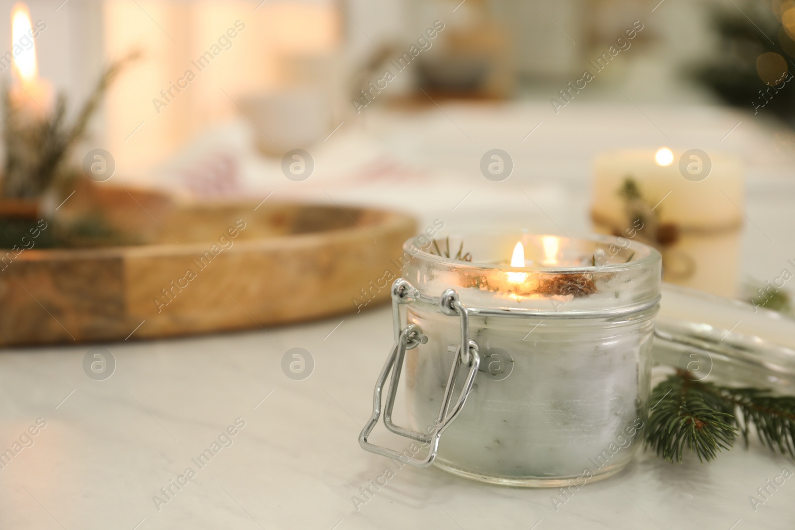 Photo of Burning scented conifer candle on white table indoors. Space for text