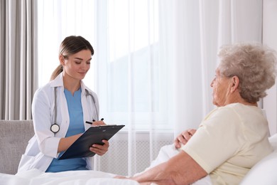Photo of Young caregiver examining senior woman in bedroom. Home health care service