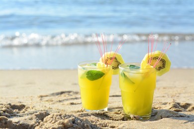 Photo of Glasses of refreshing drink with kiwi and mint on sand near sea. Space for text