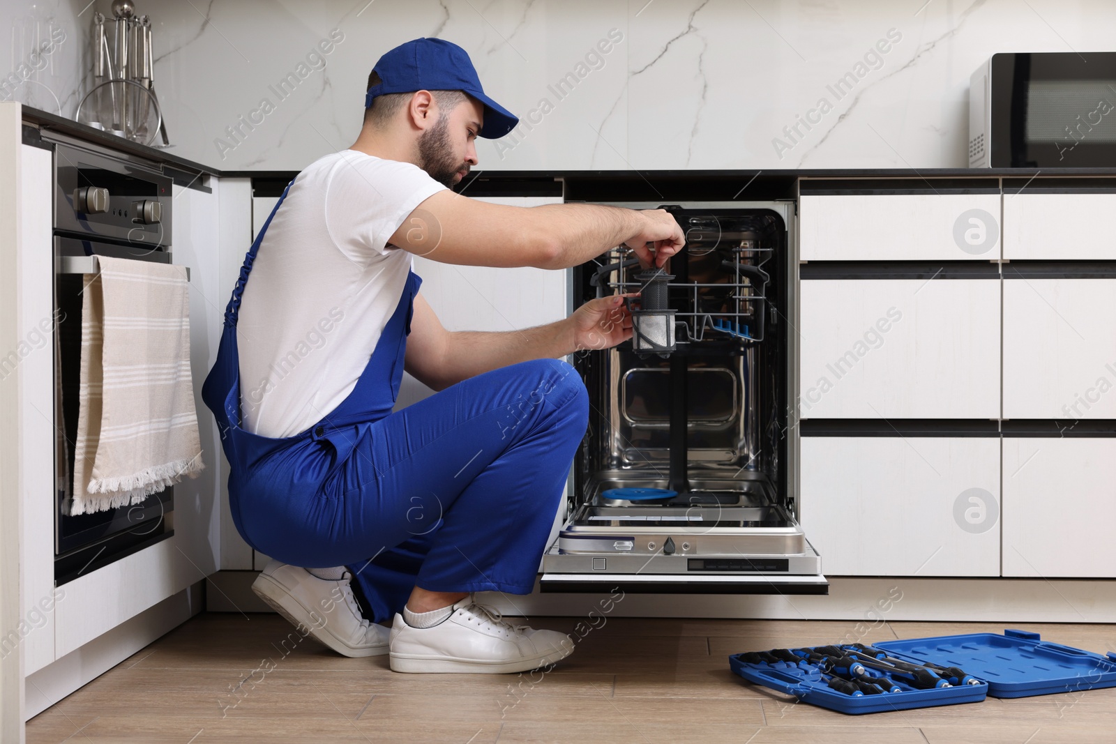 Photo of Repairman holding drain filter near dishwasher in kitchen