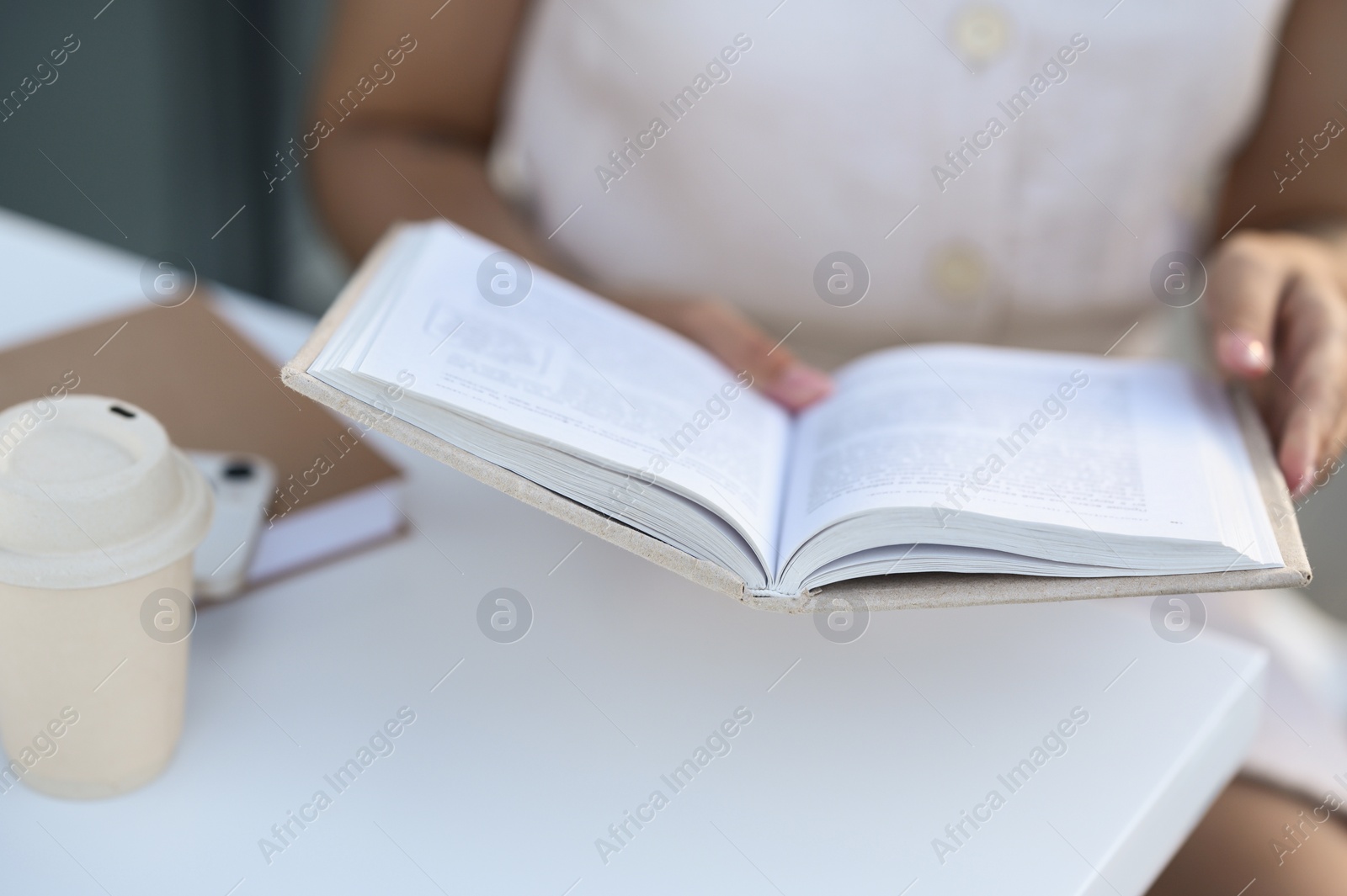 Photo of Woman with coffee reading book at white table outdoors, closeup