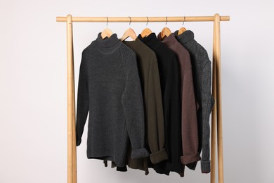 Photo of Rack with different casual sweaters on light background