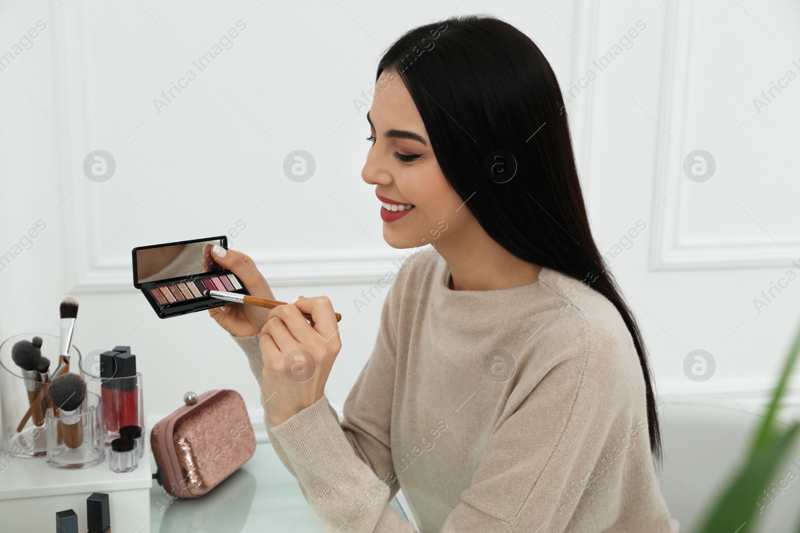 Photo of Beautiful happy woman applying makeup in room